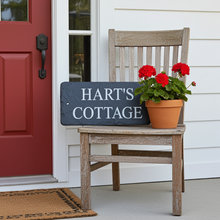 Wooden chair with a 'Hart's Cottage' sign and potted flowers on a porch.