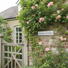 Keeper's Cottage with pink roses climbing up a brick wall and wooden gate.