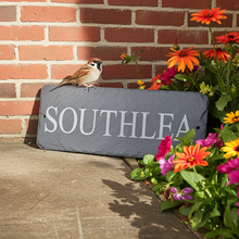 Slate nameplate with 'SOUTHLEA' on a brick wall with flowers and a bird.