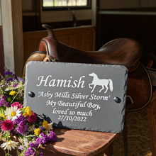 Saddle with a gray plaque featuring the name 'Hamish' and floral arrangement in an outdoor setting.
