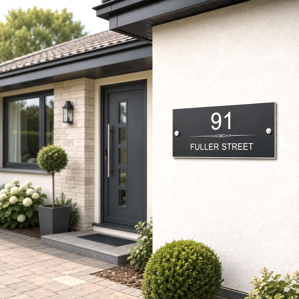 A modern black house number sign with white text reading '91 FULLER STREET' mounted on a white stucco wall of a house. The image is a high-quality render of a front porch with a dark gray door, brick wall, and landscaped shrubs.