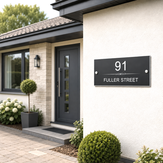 A modern black house number sign with white text reading '91 FULLER STREET' mounted on a white stucco wall of a house. The image is a high-quality render of a front porch with a dark gray door, brick wall, and landscaped shrubs.