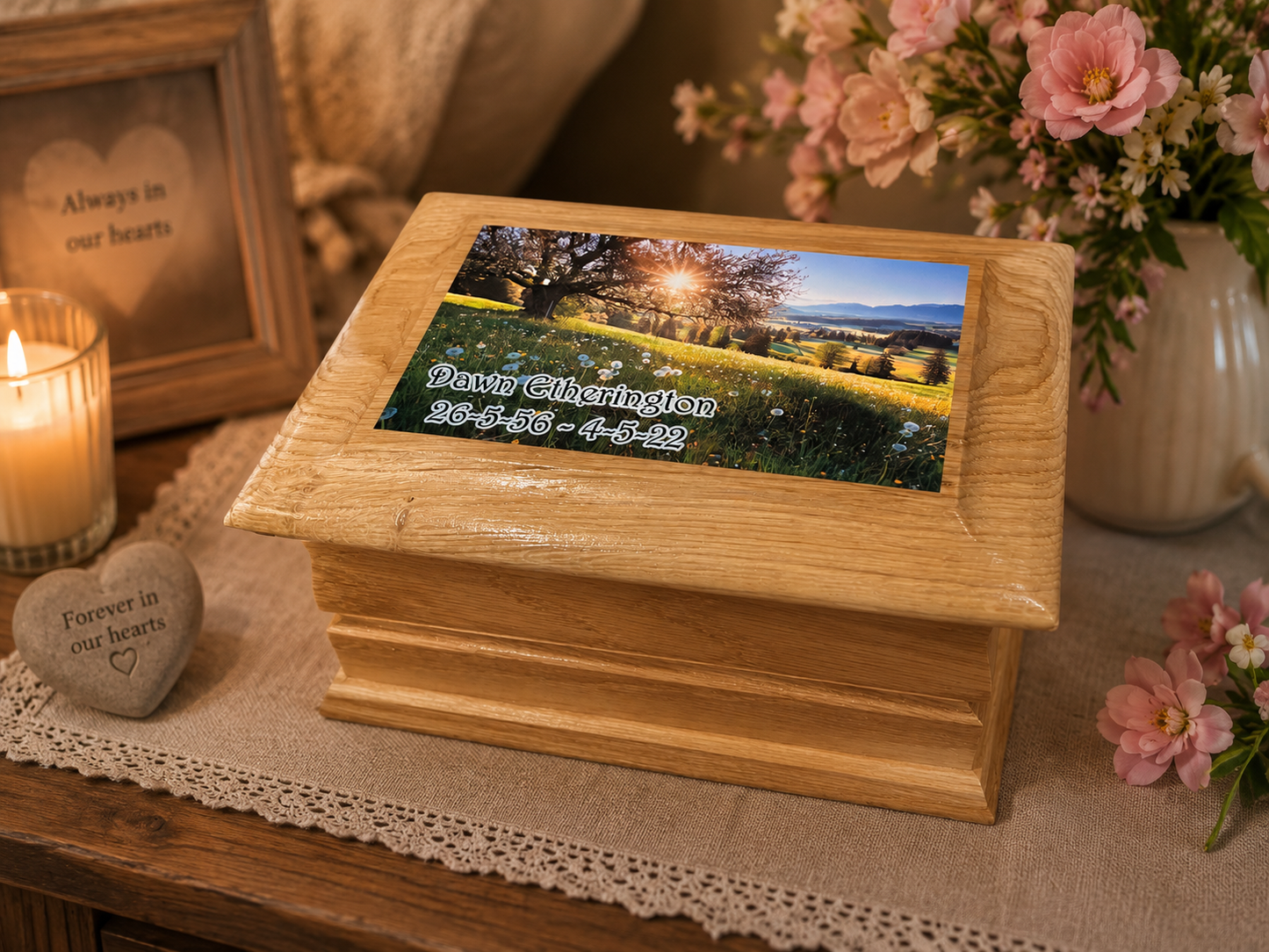 A wooden keepsake box with a custom printed photo on top, displayed on a table runner with a lit candle, flowers, and a heart-shaped remembrance stone in a warm, memorial-themed setting.
