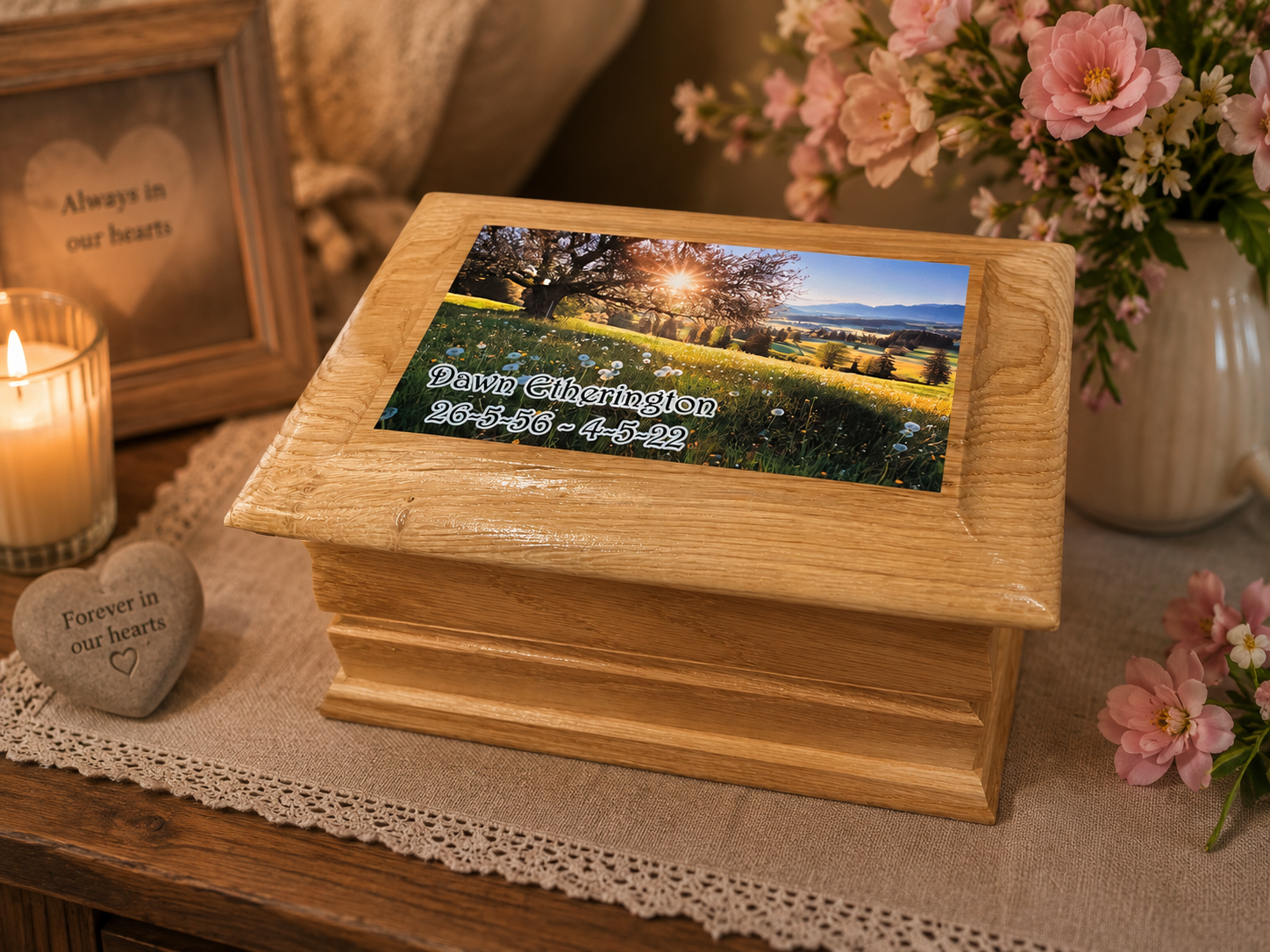 A wooden keepsake box with a custom printed photo on top, displayed on a table runner with a lit candle, flowers, and a heart-shaped remembrance stone in a warm, memorial-themed setting.