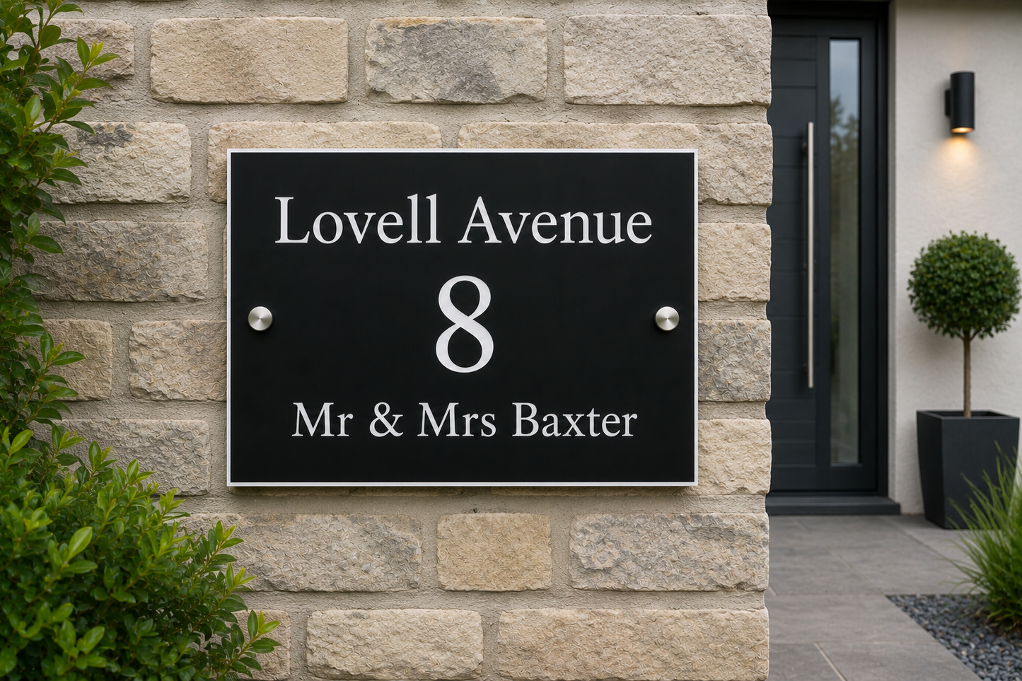 A custom black rectangular house number plaque mounted on a beige stone wall, featuring white text that reads 'Lovell Avenue', the number '8', and 'Mr & Mrs Baxter'.