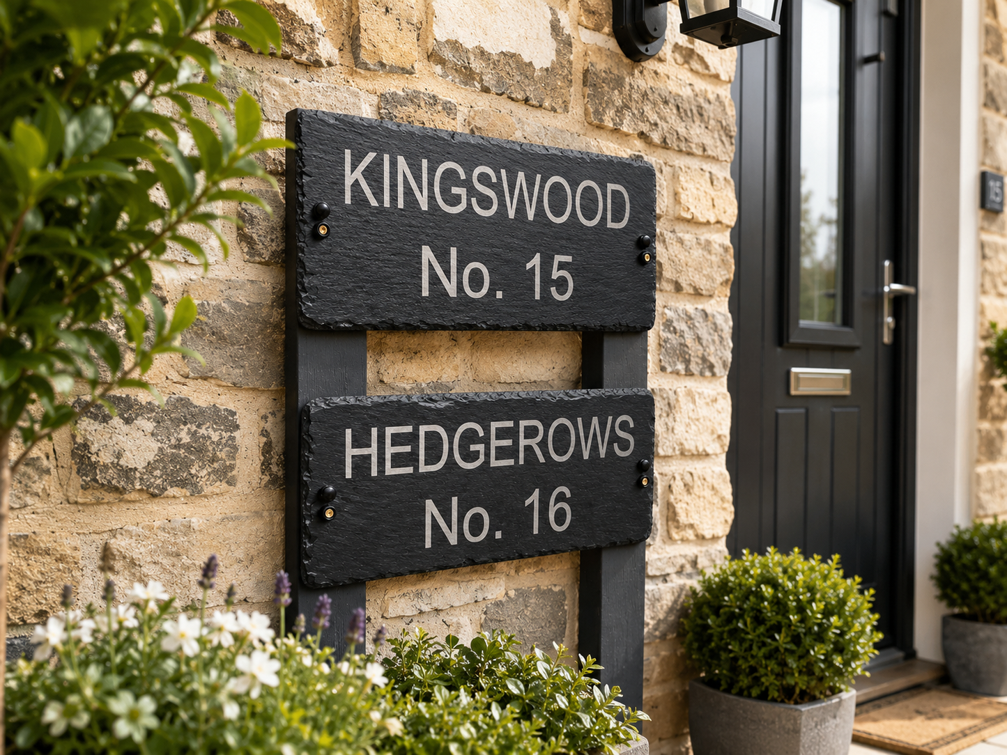 Two black rectangular house signboards mounted on a stone wall beside a dark front door. The top sign reads “KINGSWOOD No.
