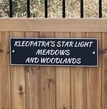 Aluminium sign with text 'KLEOPATRA'S STAR LIGHT MEADOWS AND WOODLANDS' on a wooden fence.