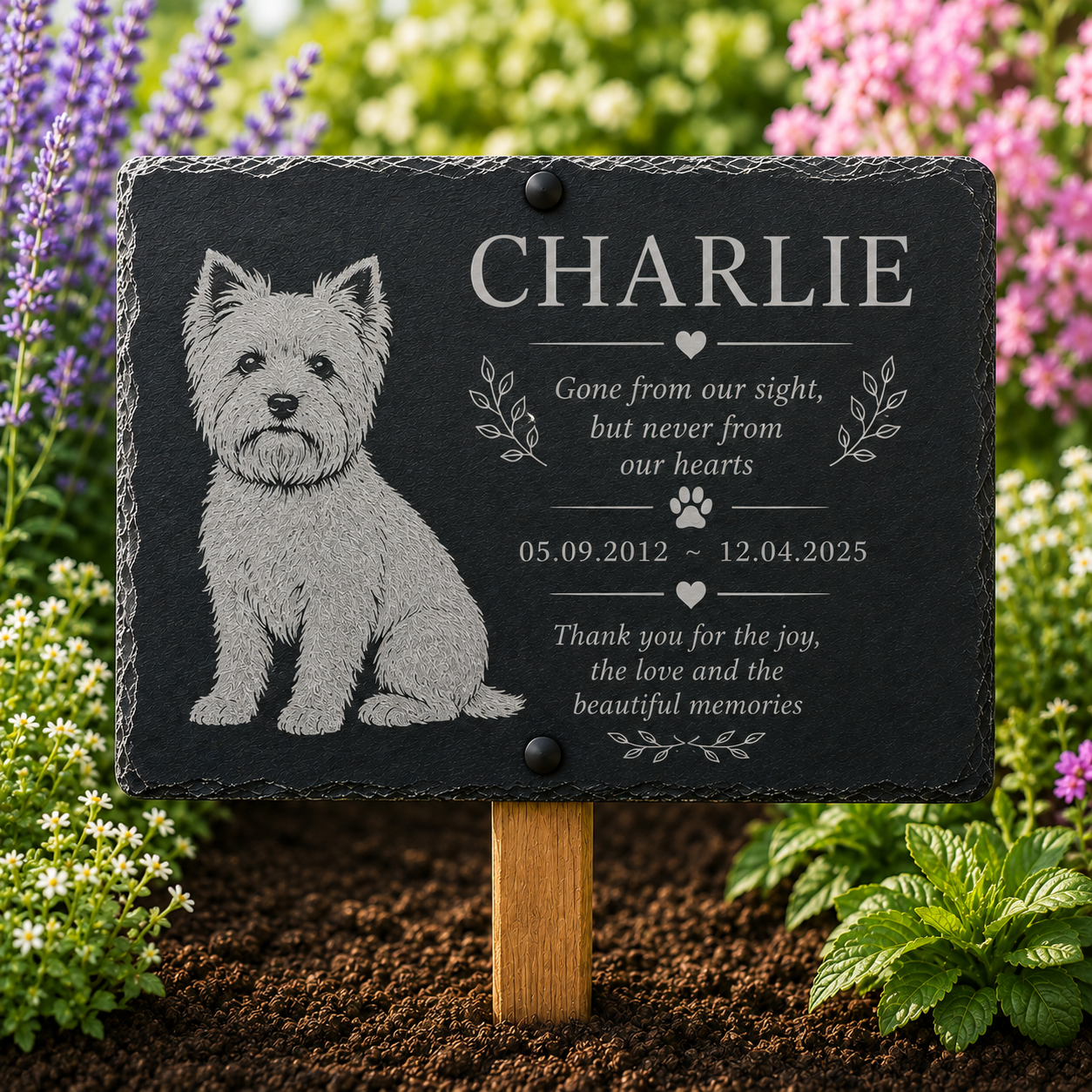 Personalized black slate pet memorial garden plaque with engraved dog portrait and text, mounted on a wooden stake in a garden bed with flowers and soil.