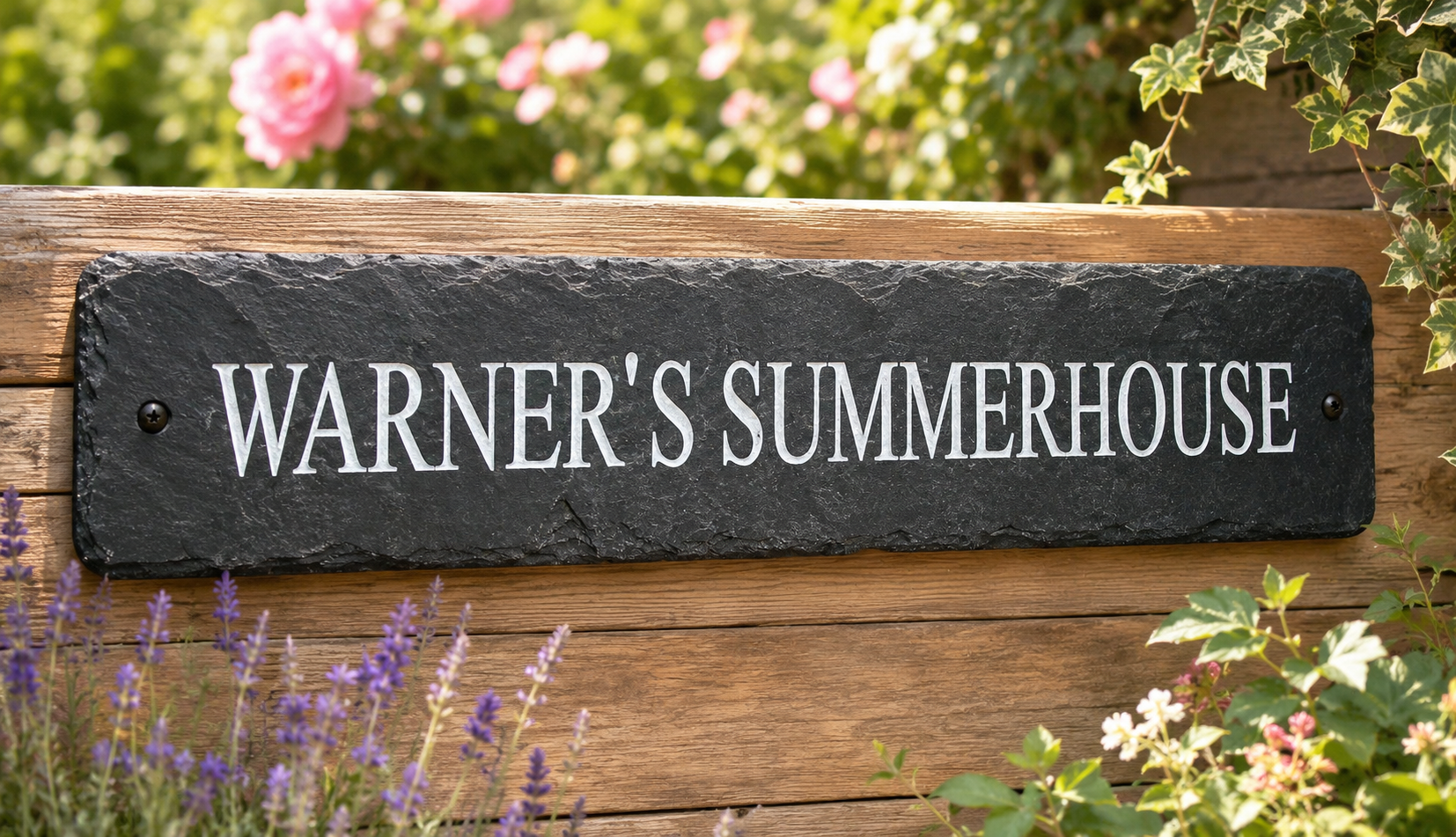 A rectangular black slate sign with white lettering that reads 'WARNER'S SUMMERHOUSE,' mounted on a wooden fence in a garden setting with flowers and greenery visible.