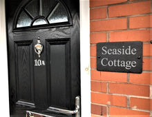 Black door with number 10A and 'Seaside Cottage' sign on brick wall