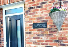 Blue/black door on a brick wall with 'EASTCOTE' sign and hanging basket.
