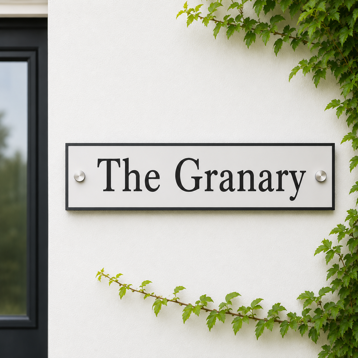 A rectangular white house sign with black lettering reading 'The Granary' mounted on a white exterior wall, framed by green ivy and next to a dark window.