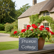 Potted red flowers with a sign reading 'Preston Cottage' in front of a stone building.