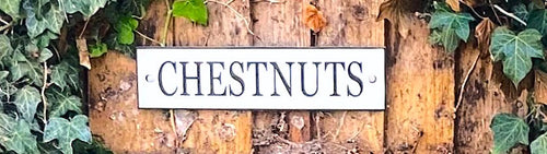 Decorative aluminium house sign with 'CHESTNUTS' text on a wooden background with ivy