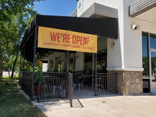 A yellow banner with text displayed on it, hanging outside a business establishment.