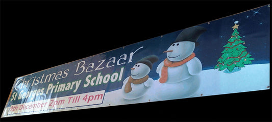 An exterior banner with full colour print, featuring cartoon characters and a Christmas tree, promoting an event at St James' Primary School.